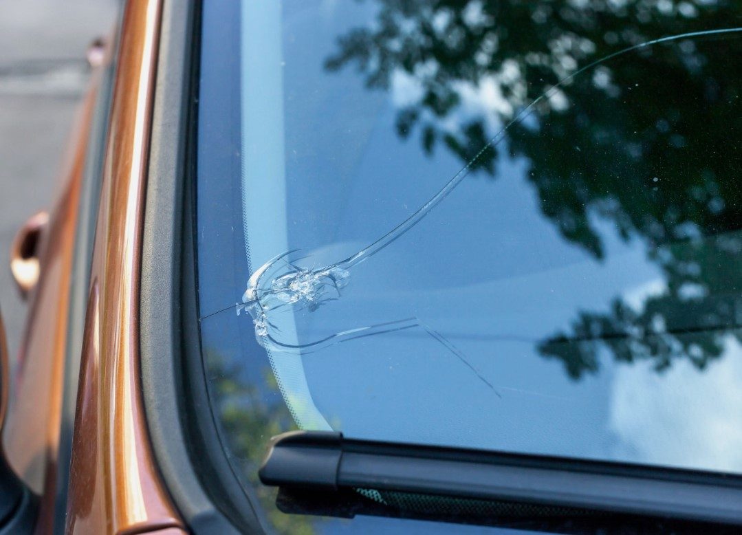 Close-up of a stone chip on a car windscreen with cracks radiating outward from the impact point