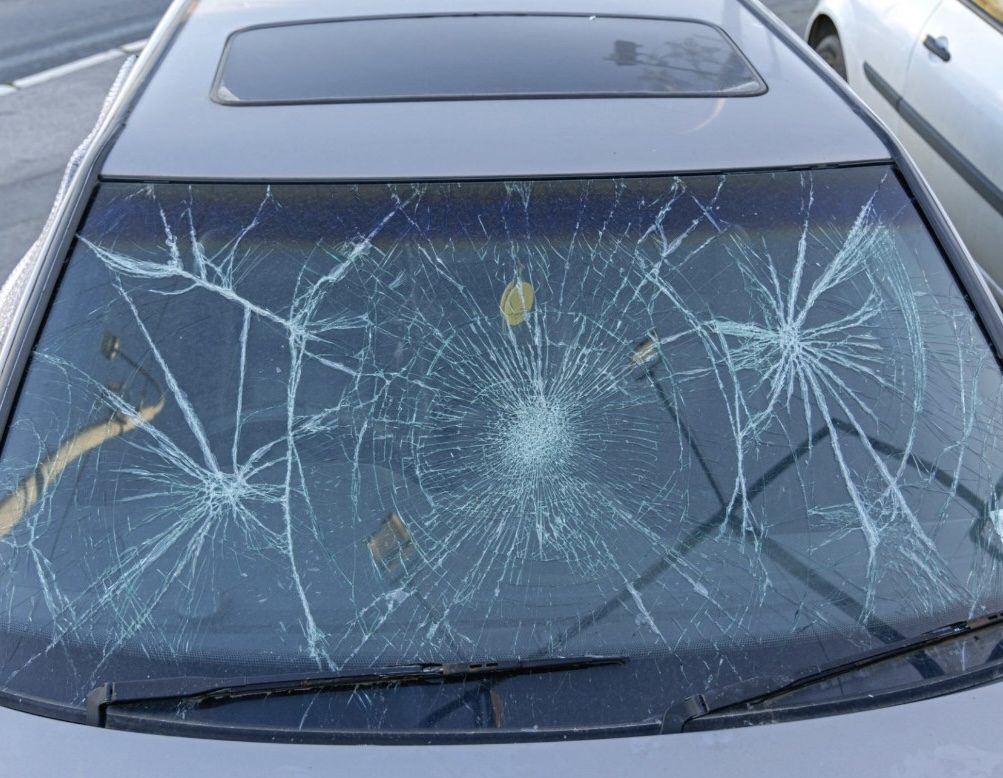 Car windscreen with a large spiderweb crack spreading across the glass from multiple impact points